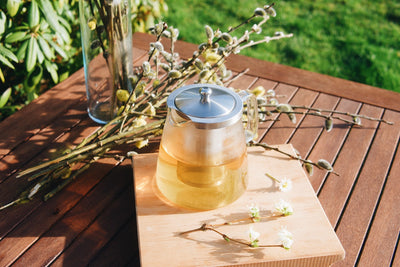Skleněná konvice na čaj Simax Charme plná čaje a jarní květiny položené na dřevěném stole