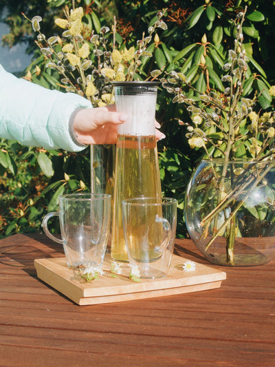 Skleněná karafa na čaj Simax Indis s čajem na dřevěném zahradním stole a dvě sklenice Simax Lyra v popředí