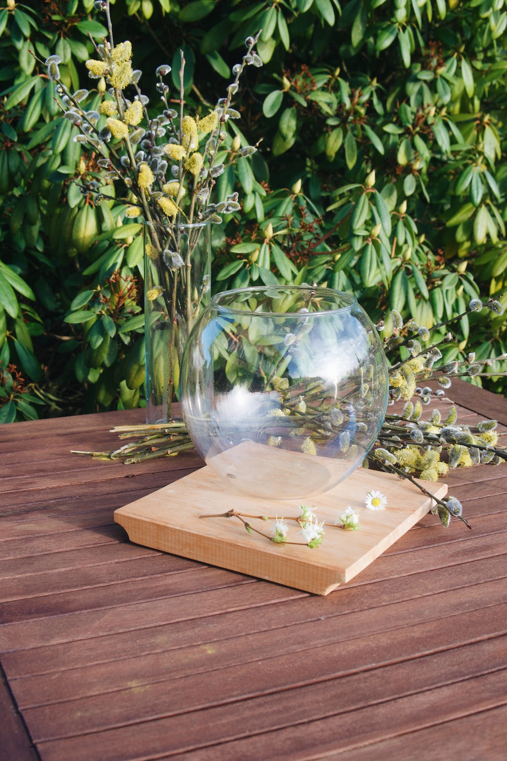 Kulatá skleněná váza Simax Globe na dřevěném zahradním stole s jarními květinami
