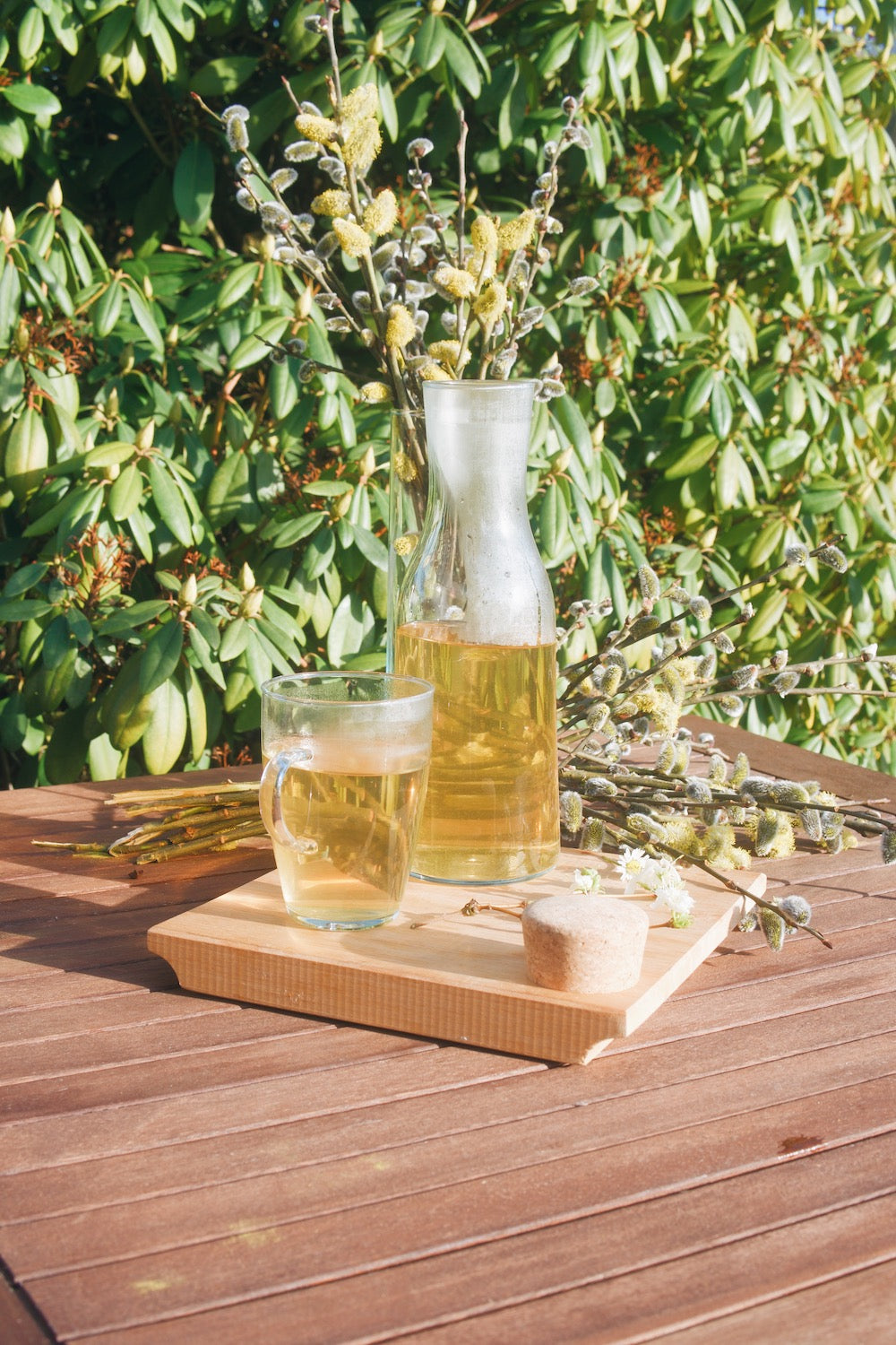 Skleněná karafa Simax Bastia a sklenice Simax Lyra plné čaje na dřevěném zahradním stole