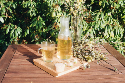 Skleněná karafa Simax Bastia s čajem a sklenice Simax Lyra postané na zahradním dřevěném stole