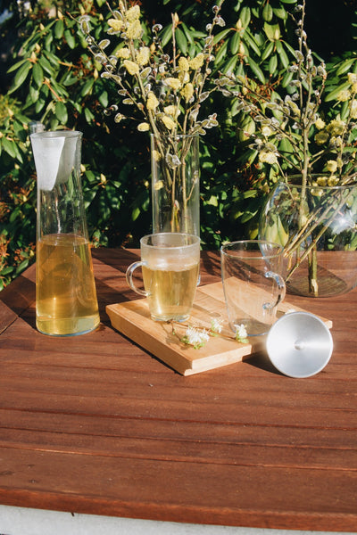 Sklenice na čaj Simax Lyra a skleněná a otevřená skleněná karafa Simax Indis na dřevěném zahradním stole