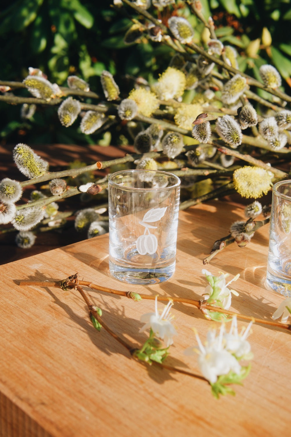 Skleněná štamprle Ateliér Žampach s pískovaným motivem švestky na dřevěném podnose s jarními květinami
