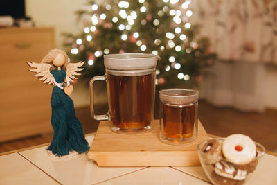 Dvoustěnný skleněný džbán Simax před vánočním stromečkem položený na stole. Vedle džbánu stojí dřevěná dekorace anděl a miska s vánočním cukrovím