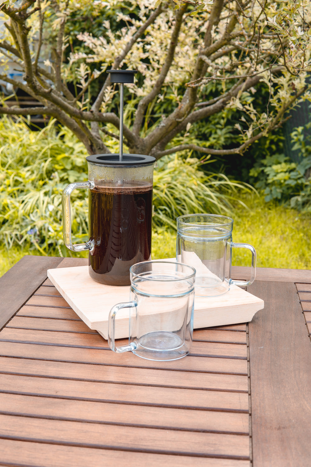 Skleněný french press Simax s kávou na zahradním stole a dvě dvoustěnné sklenice Simax Twin