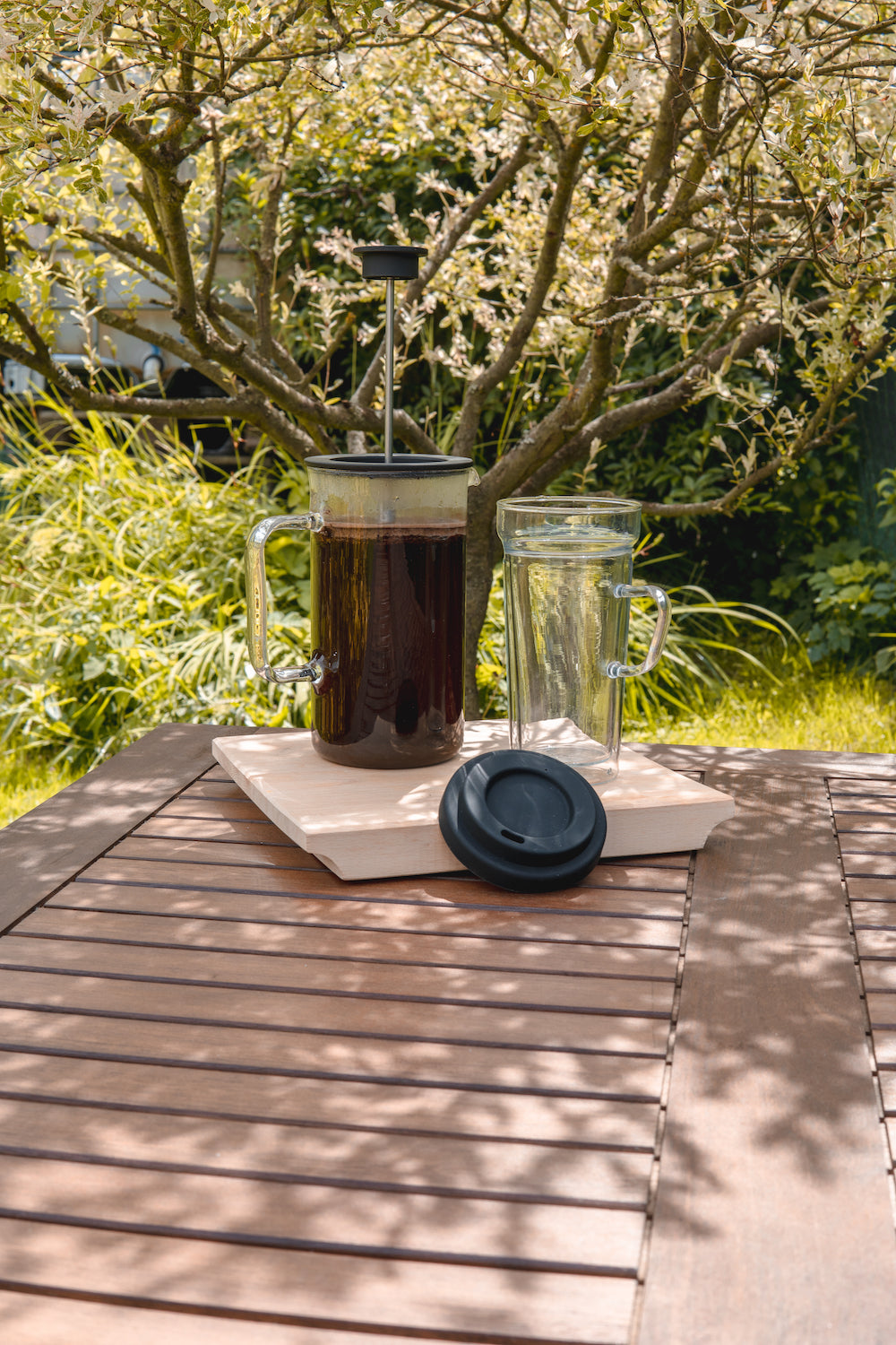Skleněný french press s kávou a dvoustěnný skleněný termo hrnek To Go na zahradním stole